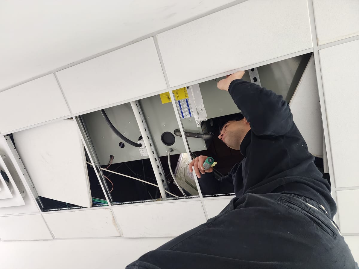 Technician working above drop ceiling tiles on HVAC unit
