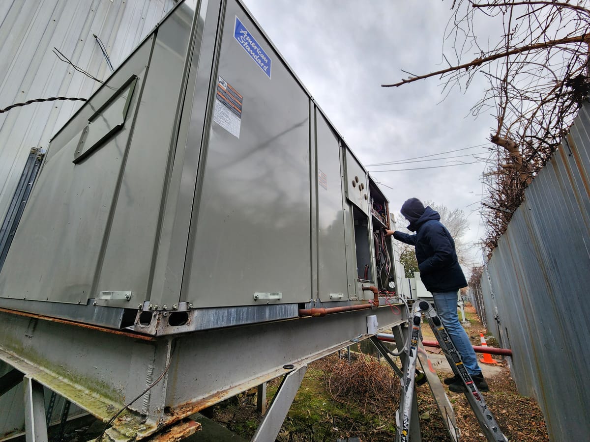 Technician servicing large commercial RTU from ladder