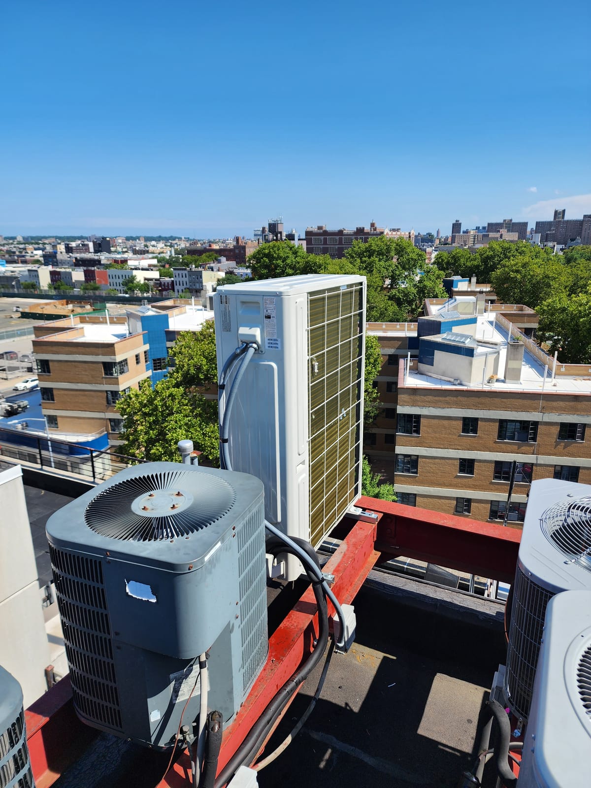 Multiple condenser units on NYC building rooftop with skyline